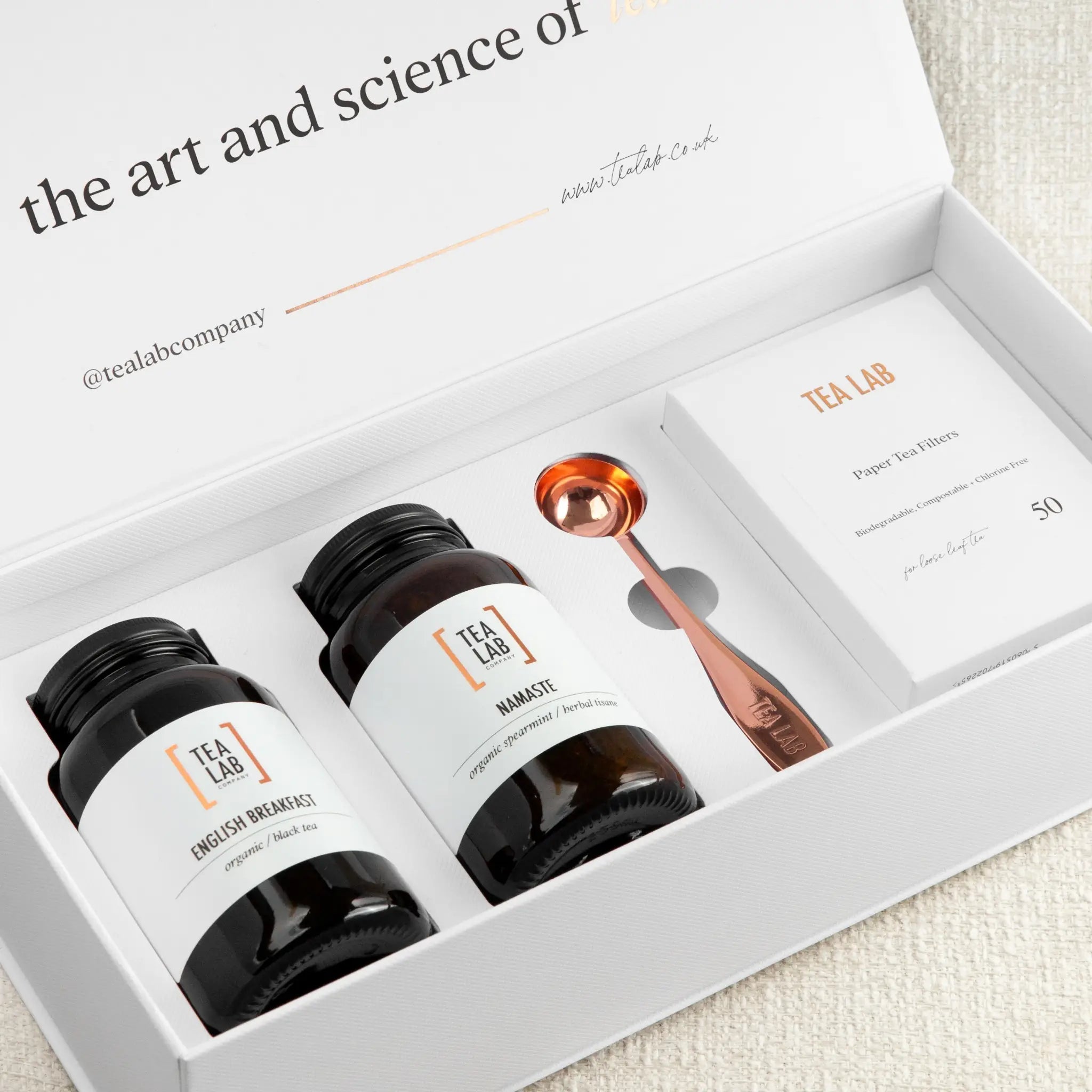 Elegant Tea Lab gift set featuring two loose leaf tea jars, a copper scoop, and eco-friendly paper tea bags presented in a white gift box
