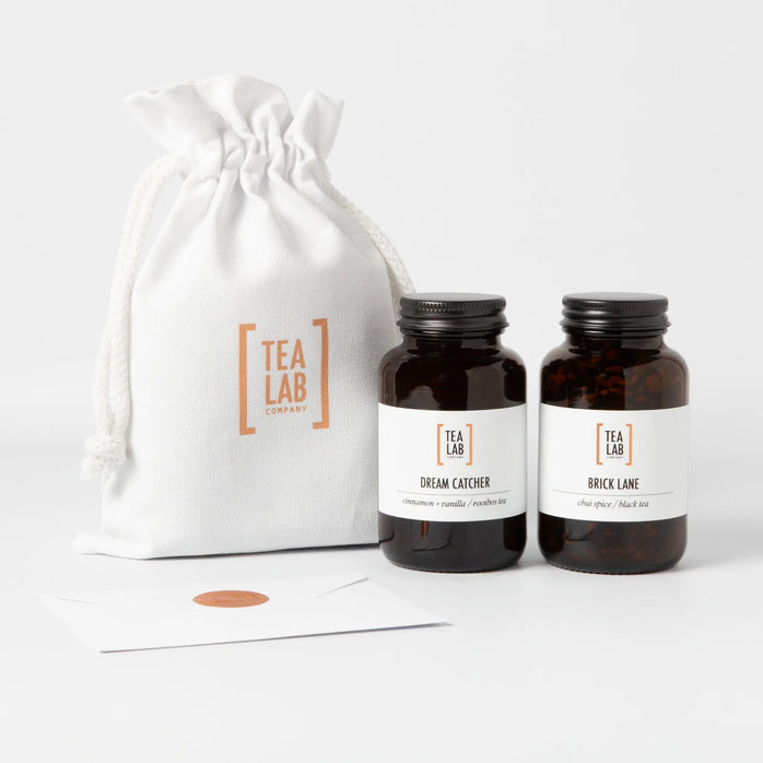 Tea Lab Mini Jar Gift Pouch featuring two amber glass jars of loose leaf tea — Dream Catcher Cinnamon and Vanilla Rooibos tea and Brick Lane Chai Spice tea — presented in a cotton drawstring pouch with fillable tea bags