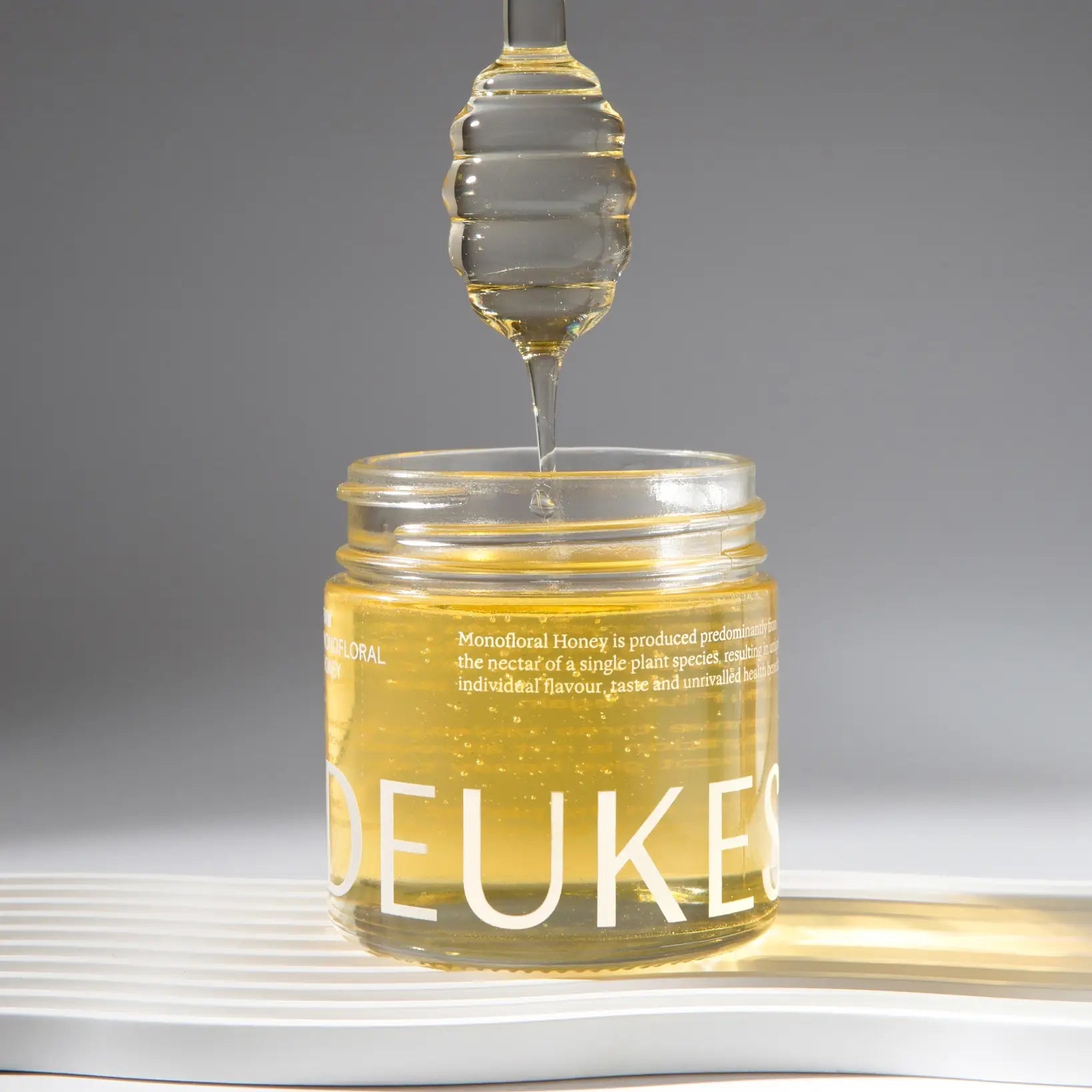 Light golden monofloral acacia honey by Deukes, shown in a glass jar with a honey dipper, part of the Tea Lab Pantry collection