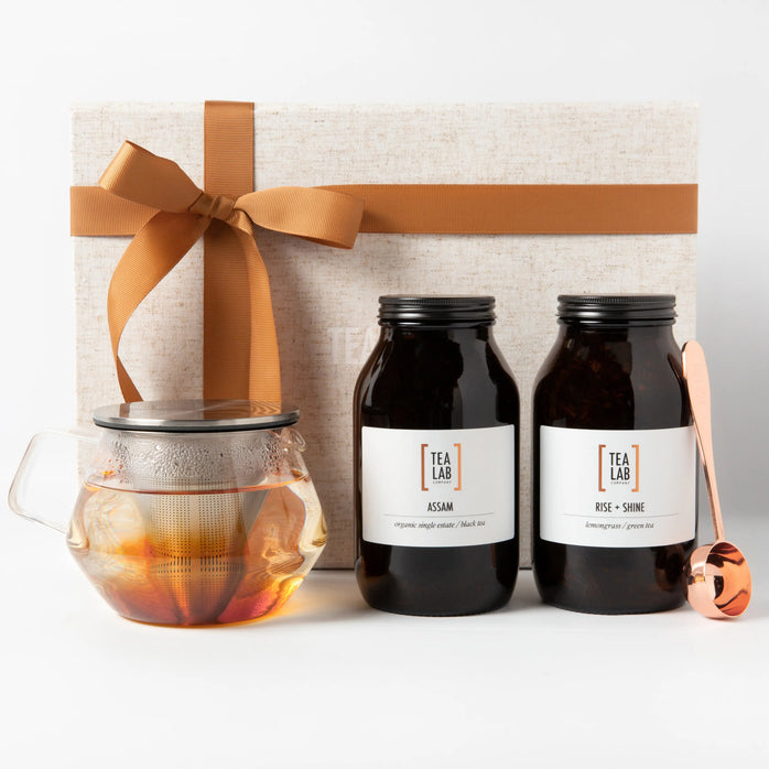 Large jars of loose leaf tea with glass kinto teapot and a copper measuring scoop packaged in a luxury linen gift box with copper riboon