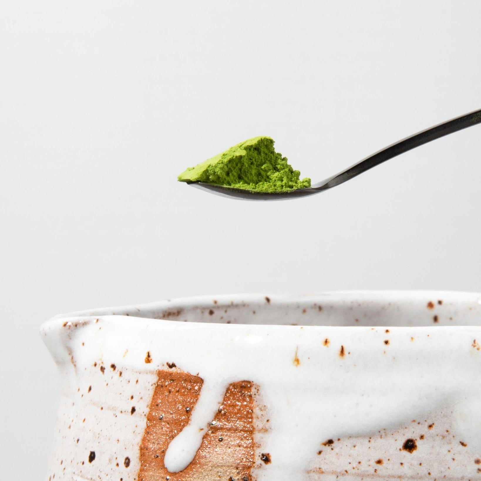 Tea Lab black matcha scoop with vibrant green matcha powder over handcrafted ceramic bowl